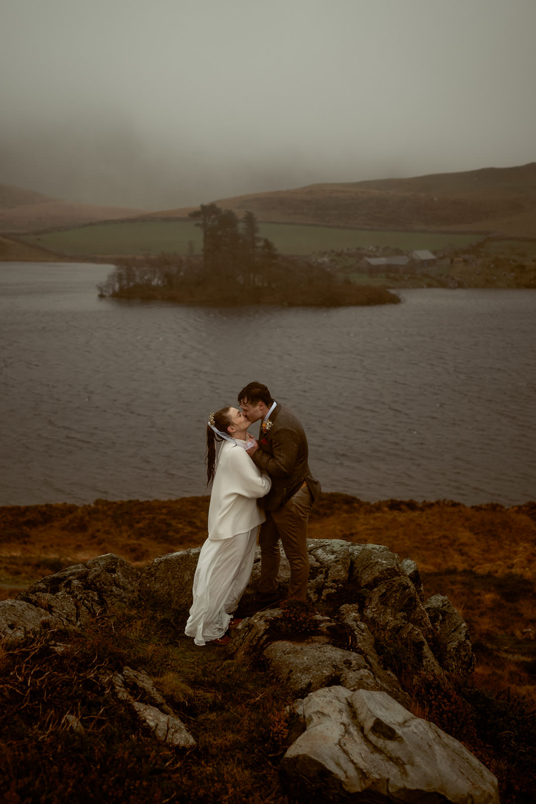 Bride in a white wedding outfit and groom standing on a rock kissing on their elopement day in South Snowdonia | Snowdonia Elopements